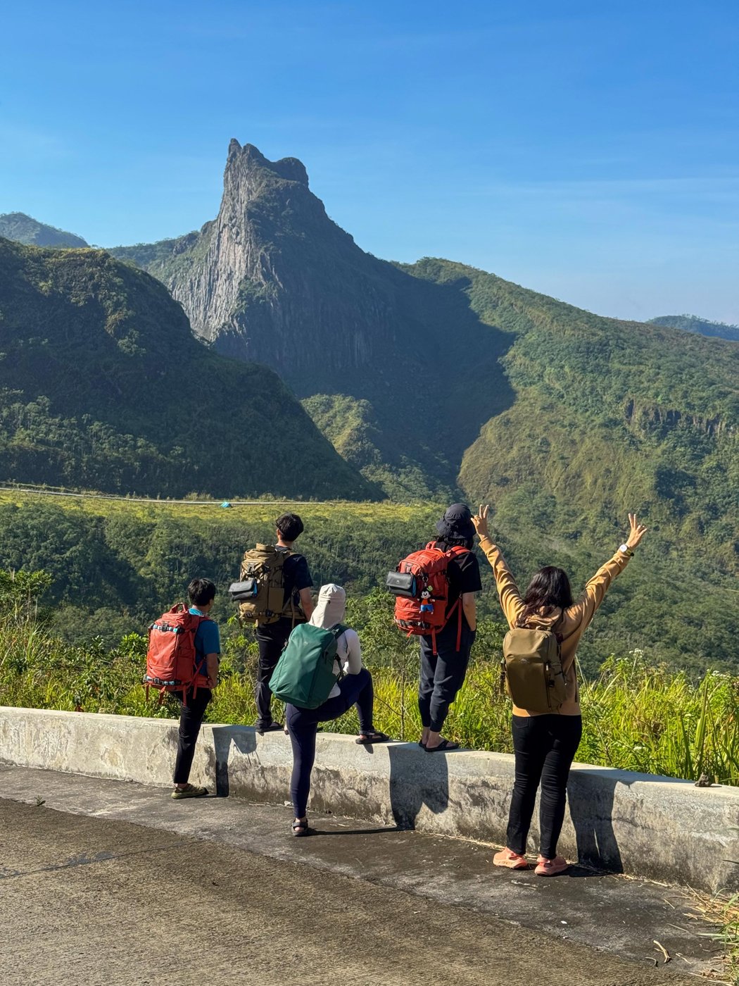 Five hikers with camera backpacks looking out at a mountain peak